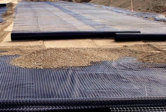 Polyester geogrid being installed on a construction site for soil reinforcement and ground stabilization over a gravel base.
