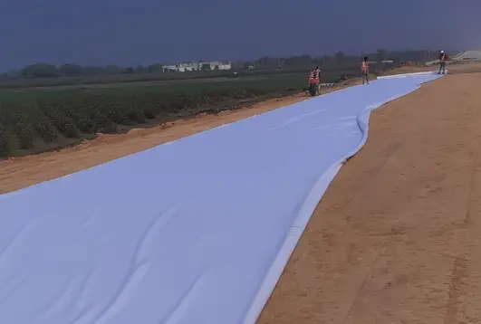 Workers laying white geotextile fabric on a construction site for soil stabilization and drainage purposes.