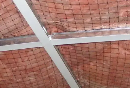 black wire mesh supporting pink fiberglass wool insulation between metal purlins in a PEB roof structure